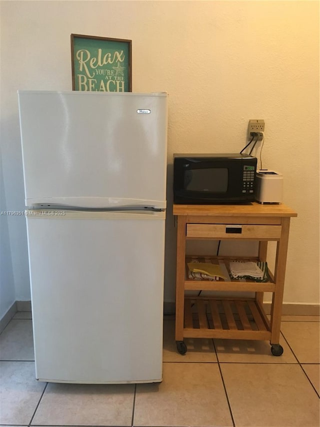 detailed view of freestanding refrigerator, black microwave, and baseboards