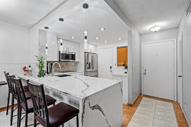 kitchen with appliances with stainless steel finishes, a peninsula, a textured ceiling, white cabinetry, and a kitchen bar