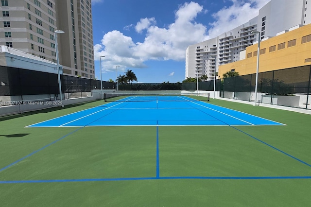 view of tennis court featuring fence, community basketball court, and a view of city