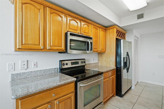 kitchen featuring stainless steel appliances, light tile patterned flooring, brown cabinets, light stone countertops, and baseboards