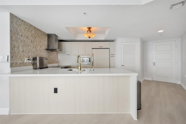 kitchen featuring wall chimney range hood, fridge, a peninsula, stainless steel microwave, and light countertops