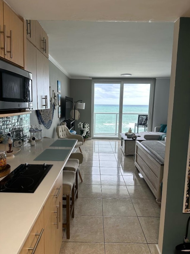19201 Collins Ave Unit 712, Sunny Isles Beach, FL 33160 - kitchen featuring stainless steel microwave, black stovetop, light tile patterned flooring, light countertops, and crown molding