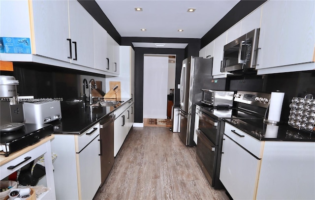 kitchen with stainless steel appliances, a sink, white cabinets, light wood-style flooring, and dark countertops