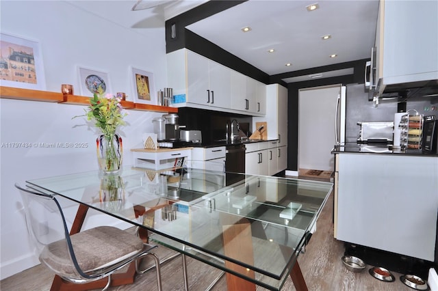 kitchen featuring wood finished floors, white cabinetry, dark countertops, a sink, and baseboards