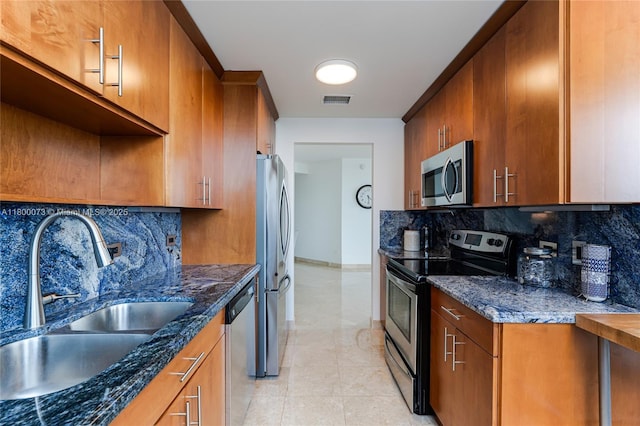 kitchen featuring appliances with stainless steel finishes, a sink, tasteful backsplash, dark stone countertops, and brown cabinets