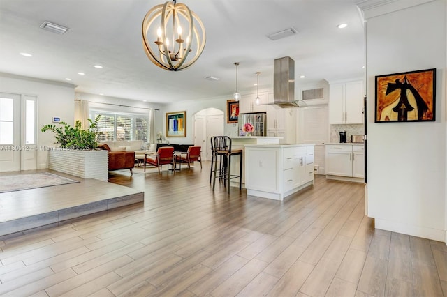 kitchen with island exhaust hood, arched walkways, open floor plan, a kitchen breakfast bar, and white cabinetry
