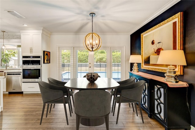 dining area featuring healthy amount of natural light, french doors, a chandelier, light wood-type flooring, and ornamental molding