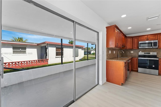 kitchen with appliances with stainless steel finishes, light wood-style flooring, a sink, backsplash, and light stone countertops