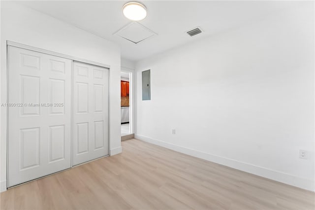 unfurnished bedroom featuring electric panel, light wood-type flooring, attic access, baseboards, and a closet