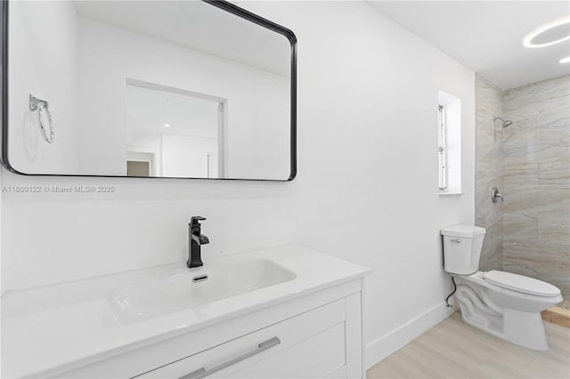 full bath featuring toilet, tiled shower, wood finished floors, vanity, and baseboards