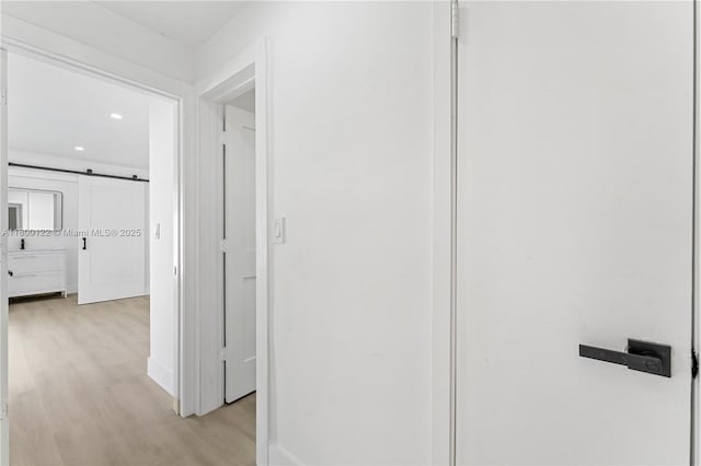 corridor with light wood-style floors, recessed lighting, a barn door, and baseboards