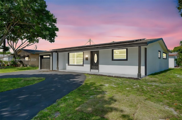 ranch-style house featuring a garage, asphalt driveway, stucco siding, and a yard