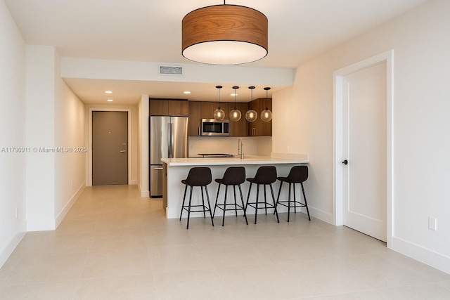 kitchen featuring appliances with stainless steel finishes, a peninsula, a kitchen bar, light countertops, and baseboards