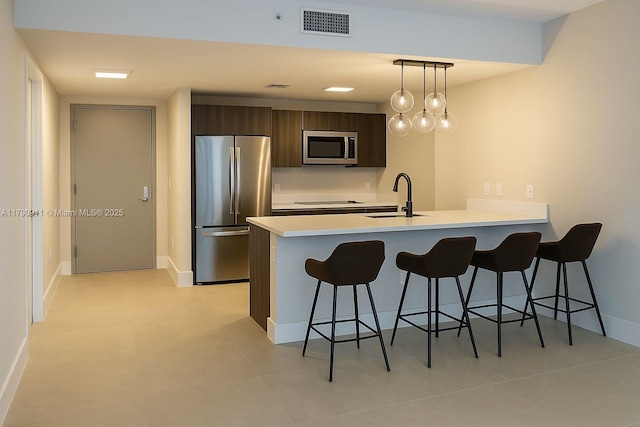 kitchen with appliances with stainless steel finishes, a sink, a kitchen bar, light countertops, and a peninsula