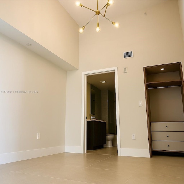 unfurnished bedroom with a high ceiling, a chandelier, baseboards, ensuite bathroom, and tile patterned flooring