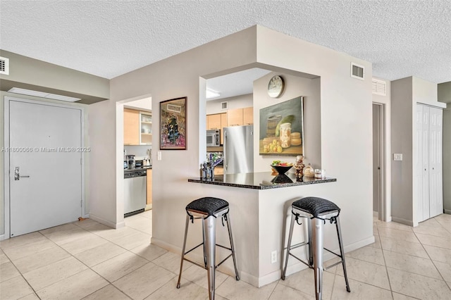 3300 NE 191st St Unit Lp04, Aventura, FL 33180 - kitchen with stainless steel appliances, light tile patterned floors, a textured ceiling, a breakfast bar area, and light brown cabinets