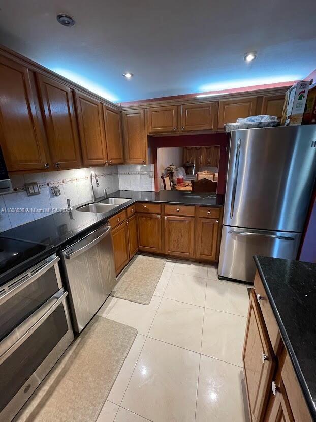 8360 Sands Point Blvd Unit G209, Tamarac, FL 33321 - kitchen featuring appliances with stainless steel finishes, a sink, decorative backsplash, brown cabinetry, and light tile patterned floors