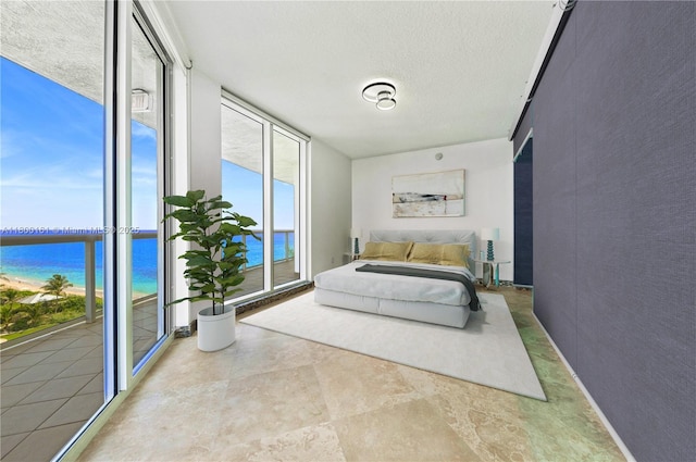 bedroom featuring a water view, floor to ceiling windows, a textured ceiling, and access to exterior