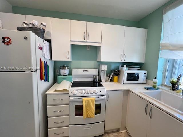 1614 Pennsylvania Ave Unit 2I, Miami Beach, FL 33139 - kitchen featuring white appliances, light countertops, white cabinets, a sink, and light wood-style flooring