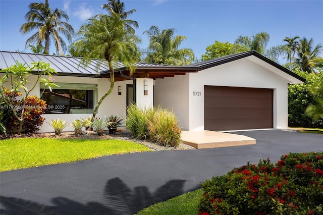 view of front facade featuring a standing seam roof, stucco siding, a garage, and asphalt driveway
