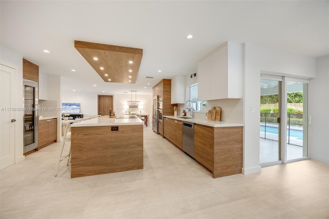 kitchen featuring modern cabinets, brown cabinetry, stainless steel appliances, light countertops, and a sink