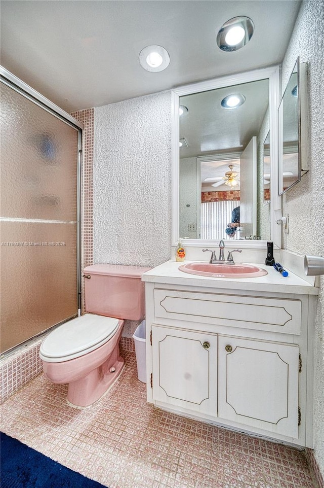 bathroom featuring a textured wall, a stall shower, vanity, toilet, and ceiling fan