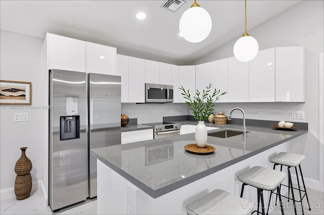 kitchen featuring appliances with stainless steel finishes, a sink, a kitchen breakfast bar, a peninsula, and decorative light fixtures