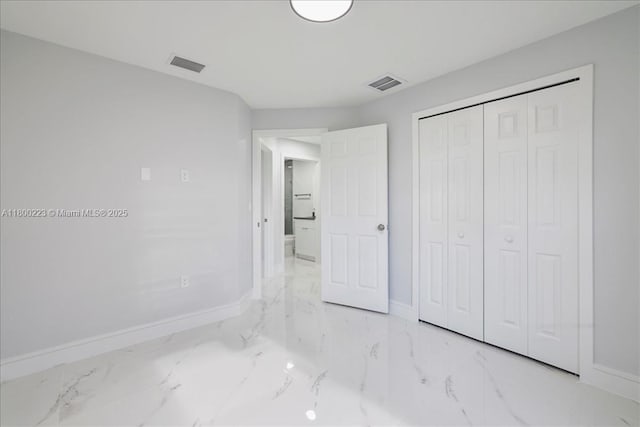 unfurnished bedroom featuring baseboards, marble finish flooring, and a closet