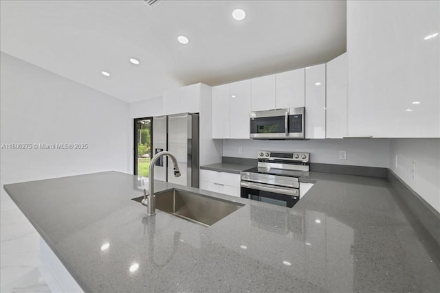 817 Moore Ave, Lehigh Acres, FL 33972 - kitchen with appliances with stainless steel finishes, a sink, white cabinetry, a peninsula, and dark stone counters