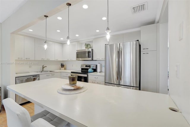 kitchen with appliances with stainless steel finishes, a sink, a breakfast bar, light countertops, and pendant lighting