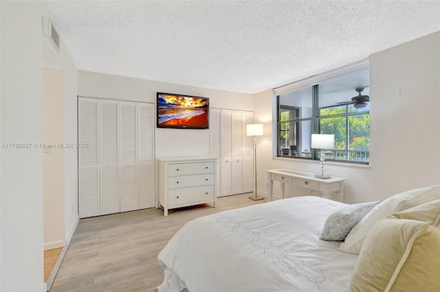 bedroom featuring multiple closets, light wood finished floors, a textured ceiling, and baseboards