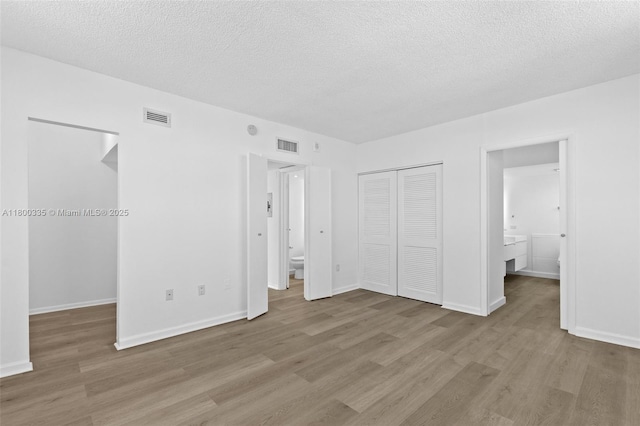 6900 Bay Dr Unit 10I, Miami Beach, FL 33141 - unfurnished bedroom with a closet, wood finished floors, connected bathroom, a textured ceiling, and baseboards