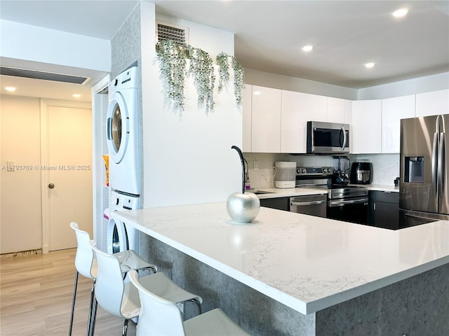 3731 N Country Club Dr Unit 2228, Aventura, FL 33180 - kitchen featuring appliances with stainless steel finishes, stacked washer / dryer, light wood-type flooring, a breakfast bar, and white cabinetry