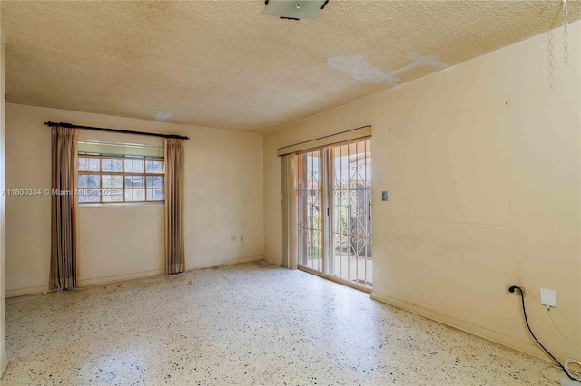 empty room with a textured ceiling, baseboards, and speckled floor
