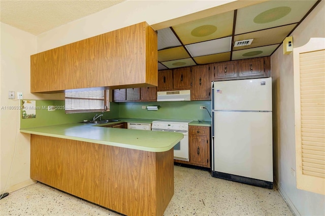 kitchen with white appliances, under cabinet range hood, a peninsula, a sink, and baseboards