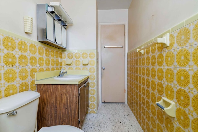 half bathroom featuring tile walls, wainscoting, toilet, vanity, and speckled floor