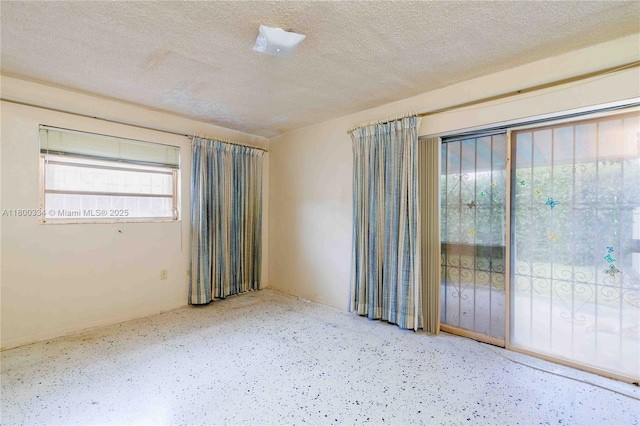 empty room featuring a textured ceiling, speckle patterned floor, and baseboards
