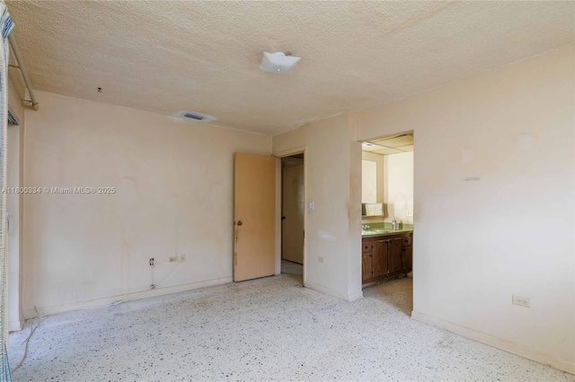 empty room featuring baseboards, a textured ceiling, a sink, and dark speckled floor