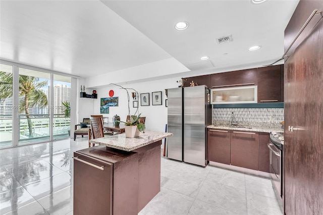 kitchen with appliances with stainless steel finishes, a wall of windows, tasteful backsplash, a kitchen island, and a sink