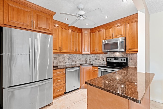 kitchen featuring stainless steel appliances, a sink, a peninsula, dark stone counters, and decorative backsplash
