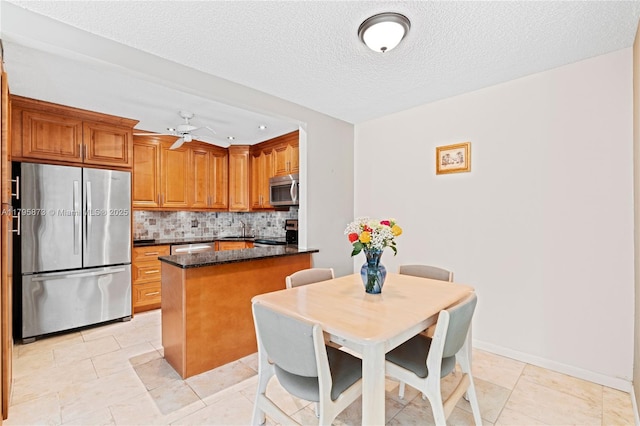 kitchen featuring stainless steel appliances, backsplash, brown cabinetry, ceiling fan, and a textured ceiling