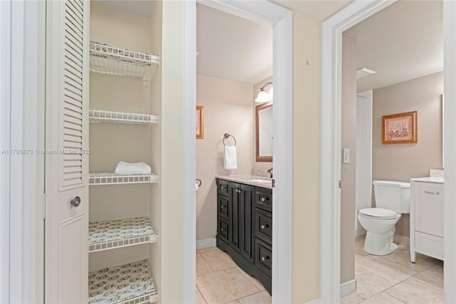 bathroom featuring tile patterned floors, toilet, vanity, baseboards, and a spacious closet