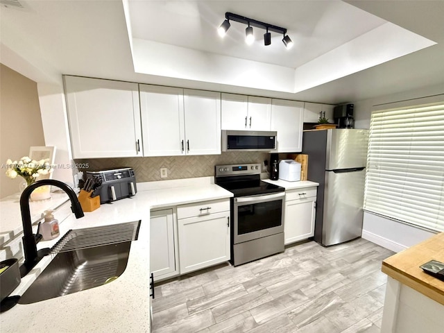 300 Promenade Dr Unit 105, Dunedin, FL 34698 - kitchen featuring stainless steel appliances, a sink, a tray ceiling, light countertops, and decorative backsplash