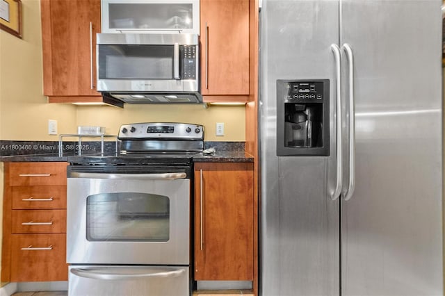kitchen with appliances with stainless steel finishes, brown cabinets, and dark stone counters