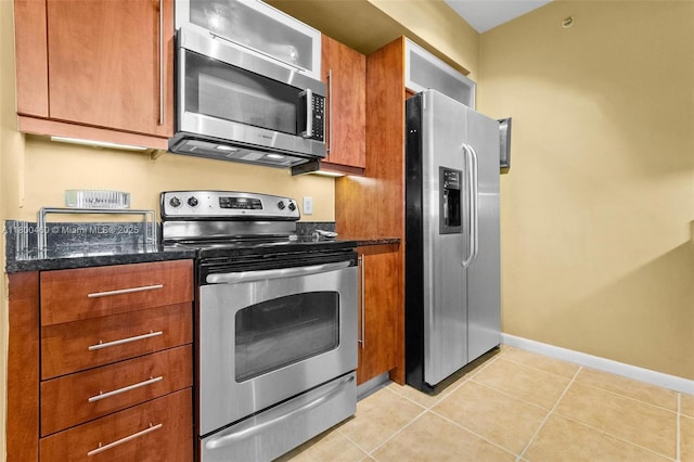 kitchen with appliances with stainless steel finishes, brown cabinets, light tile patterned floors, and dark stone counters
