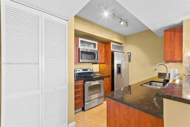 kitchen featuring appliances with stainless steel finishes, a sink, light tile patterned flooring, brown cabinets, and track lighting