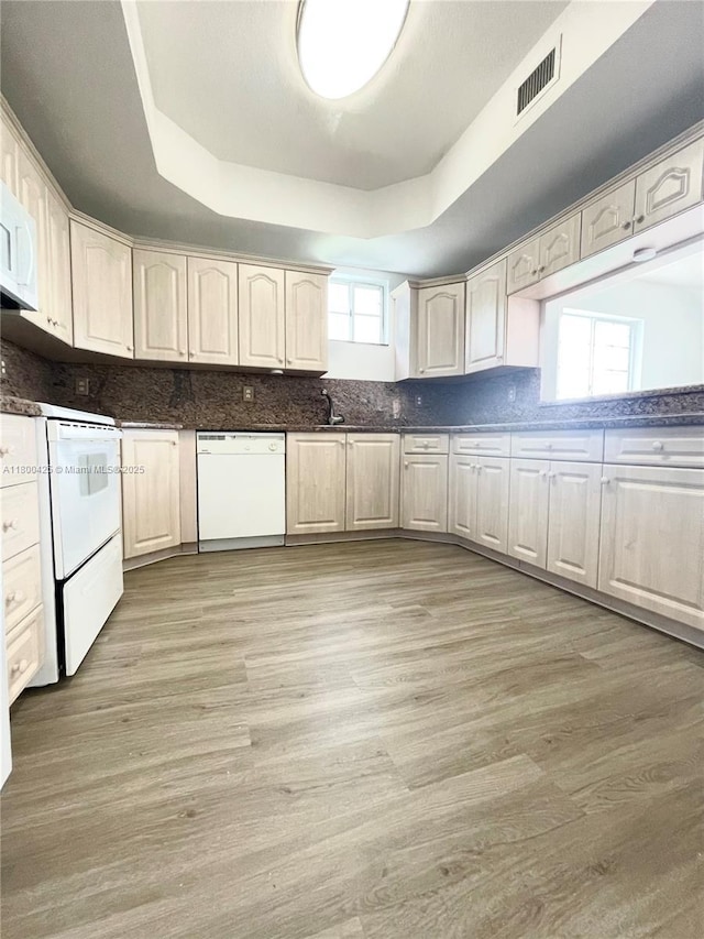 kitchen with white appliances, a tray ceiling, decorative backsplash, light wood-style floors, and dark countertops