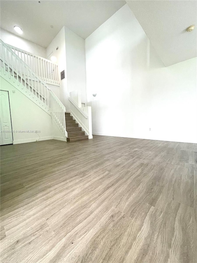 unfurnished living room featuring stairs, wood finished floors, and baseboards