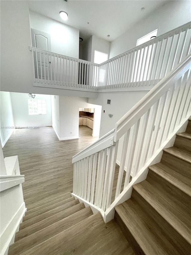 staircase featuring wood finished floors, baseboards, and a towering ceiling