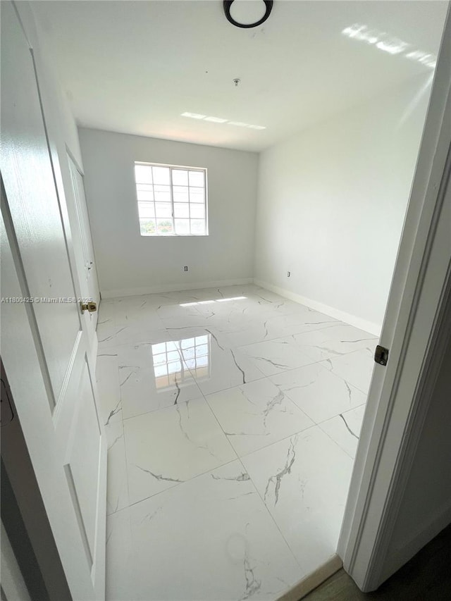 empty room with marble look tile flooring and baseboards
